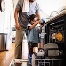 A dad helps his daughter load the dishwasher.