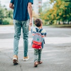 A dad walks his small child to school as they hold hands.
