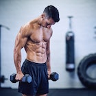 A fit, shirtless man with defined muscles holding dumbbells.