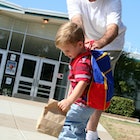 Young child wearing backpacking outside of school pulling away while his dad tries to control him.