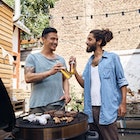 Two men drinking beer at a cookout while grilling meat.