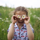 A child holding flowers up to her eyes, the simplest form of a spring joke for kids.