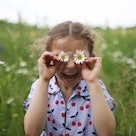 A child holding flowers up to her eyes, the simplest form of a spring joke for kids.