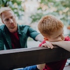 A father consoling his upset son as they sit on a bench in a park.