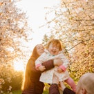 A parent holding their baby girl while surrounded by flowering trees.