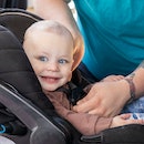 Happy baby is smiling while being buckled into car seat in family car