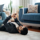 Man stretches his feet on the sofa and looks at the phone while lying on the floor