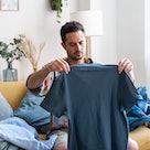 Middle aged man folding t-shirt while sitting on the couch