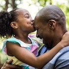 A girl kissing her bald father's head.