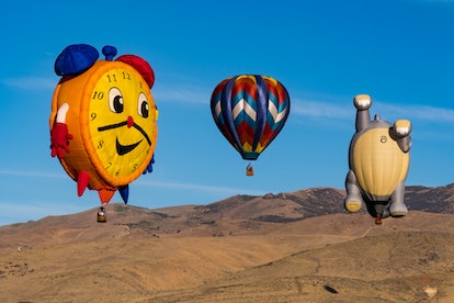 A clock-shaped, a cat-shaped, and a regular-shaped hot air balloon in the sky