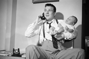 1950s distressed father holding baby while talking on telephone. (Photo by Debrocke/ClassicStock/Get...