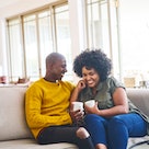 Husband and wife sitting on the couch with coffee, having a happy conversation and laughing