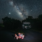 A family on an RV trip stargazes at night, lying on their backs and staring up at the night sky.