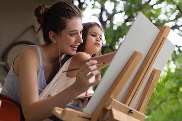 Young woman with her daughter painting on easel.