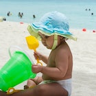 An August baby sitting on a beach, playing with a bucket and shovel.