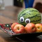 Melon with googly eyes, sitting in a bowl intimidating some apples