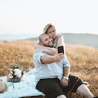 A fat man on a picnic with a woman outdoors in nature, taking a selfie.