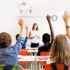 School kids in classroom raising their hands.