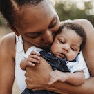 A Black mom holding and kissing her baby.