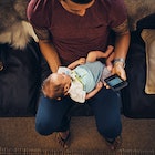 A man holding a baby while sitting on a couch and looking at his phone.