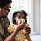 A dad blowing his sick daughter's nose with a tissue.