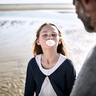 A daughter chews gum and blows a bubble on the beach as her dad watches.