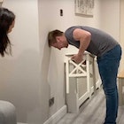 A man attempts the chair challenge at home while his wife looks on.