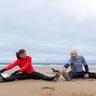 A mature couple sitting on Tynemouth Beach and stretching before going surfing. They are both wearin...