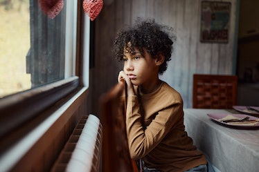 A sad child with low self-esteem staring out a window.