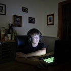 A white boy in the dark playing video games on a computer.