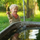 Happy little boy throwing rocks into the rainwater tank in the garden. Stone skipping game.