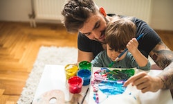 A dad helping his child paint artwork.