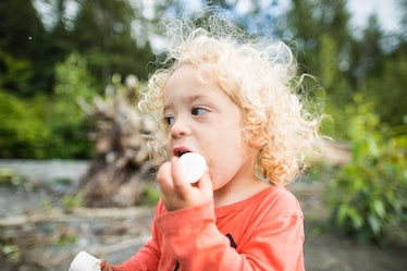 A child eating marshmallows outdoors near a lake.