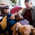 Two dads on a couch with their son, smiling.
