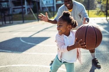 A girl playing basketball with her dad