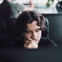 Man with long hair sitting at computer thinking