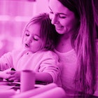 pink photo edit of a young girl working on construction paper crafts while sitting in her mother's l...